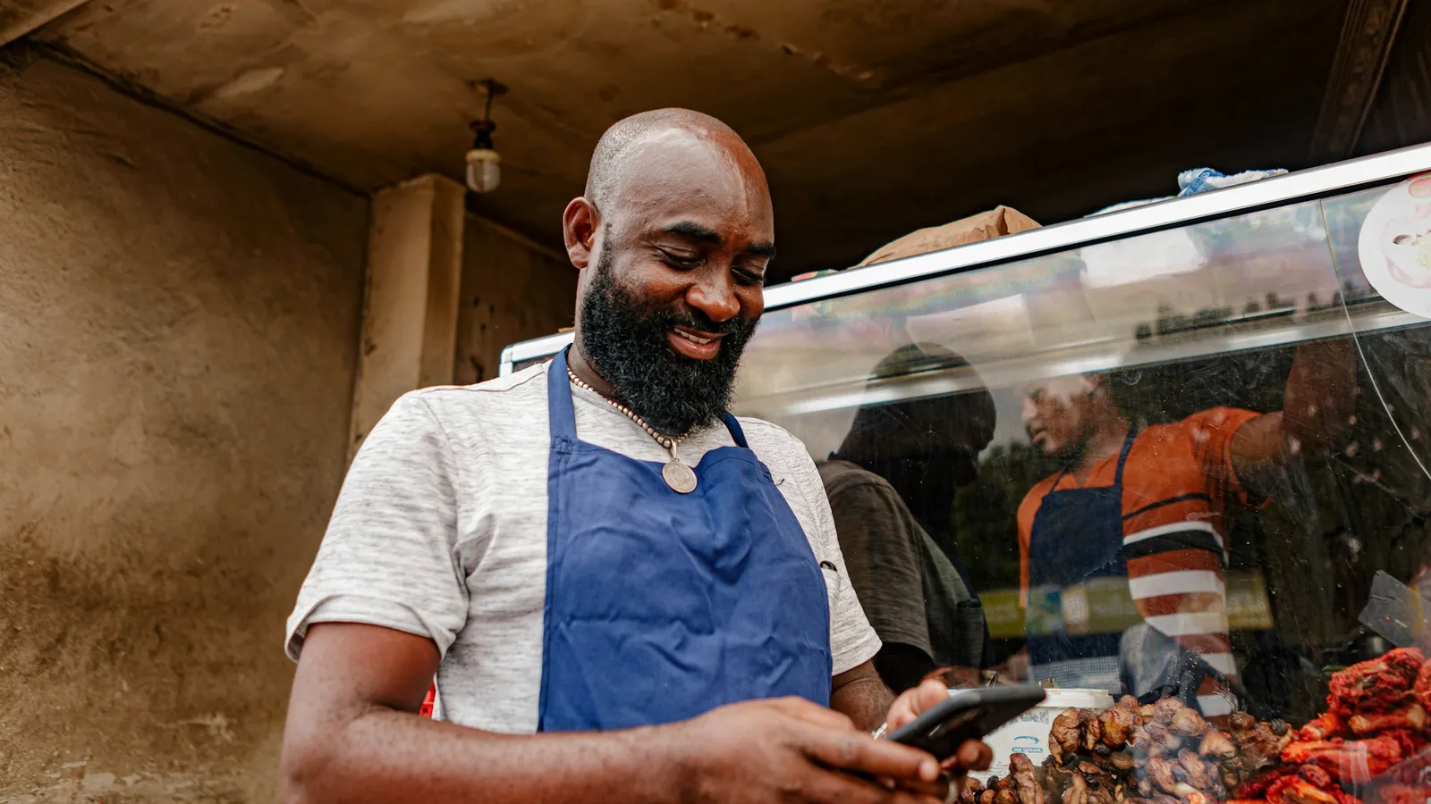 Small business owner in an apron checking his phone at his shop counter