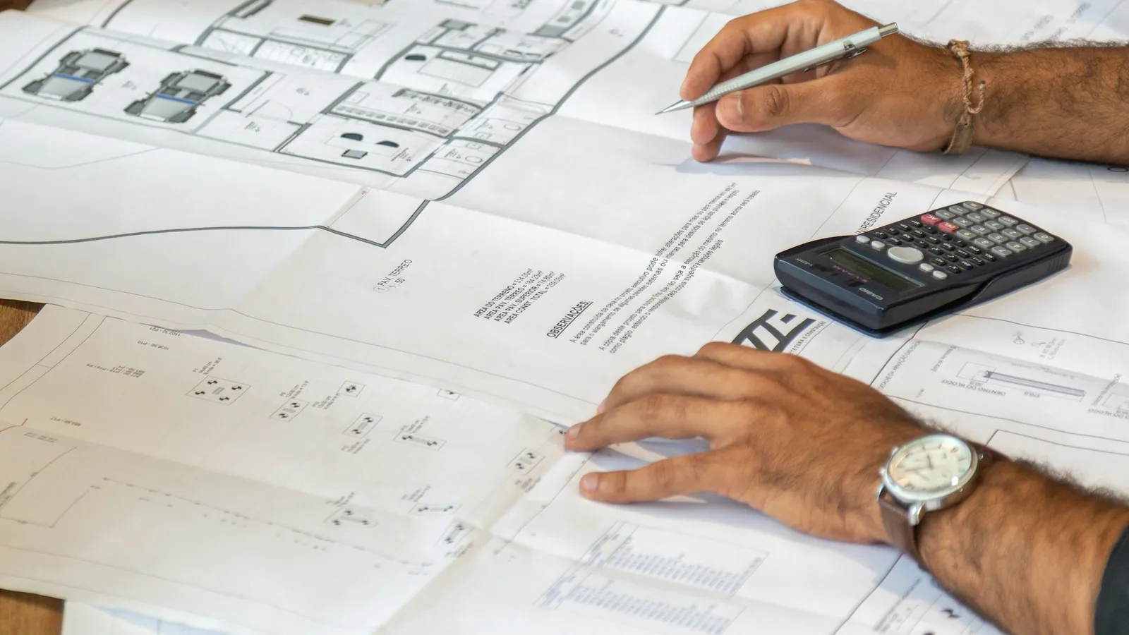Hands working through building plans with a calculator and pencil