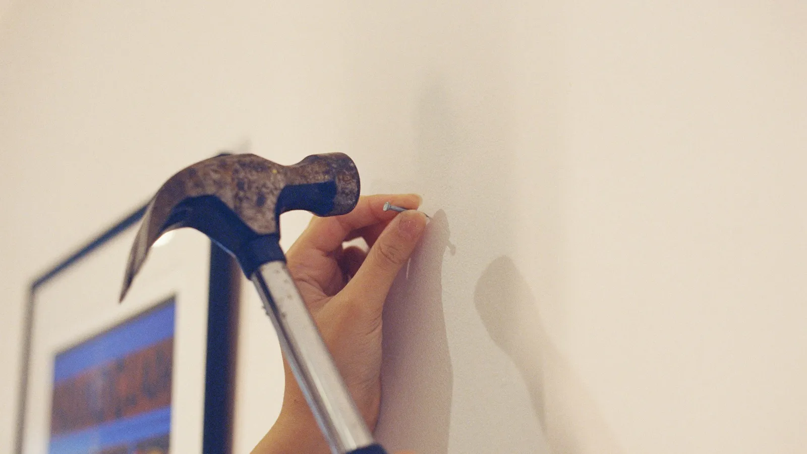 Hand holding a nail against a wall with a hammer raised