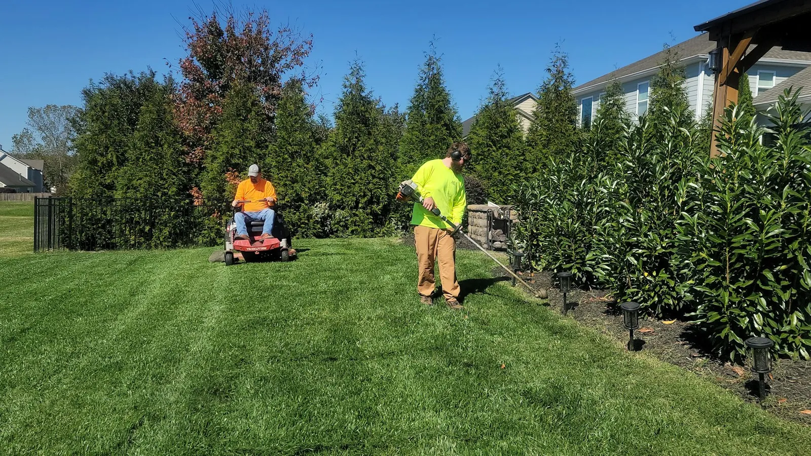 Two lawn care workers mowing and trimming a large green lawn on a sunny day