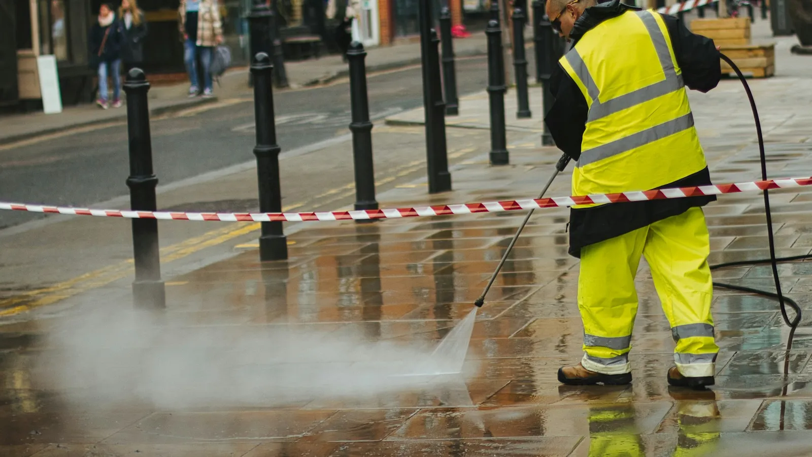 Worker in a yellow safety jacket cleaning pavement with a pressure washer